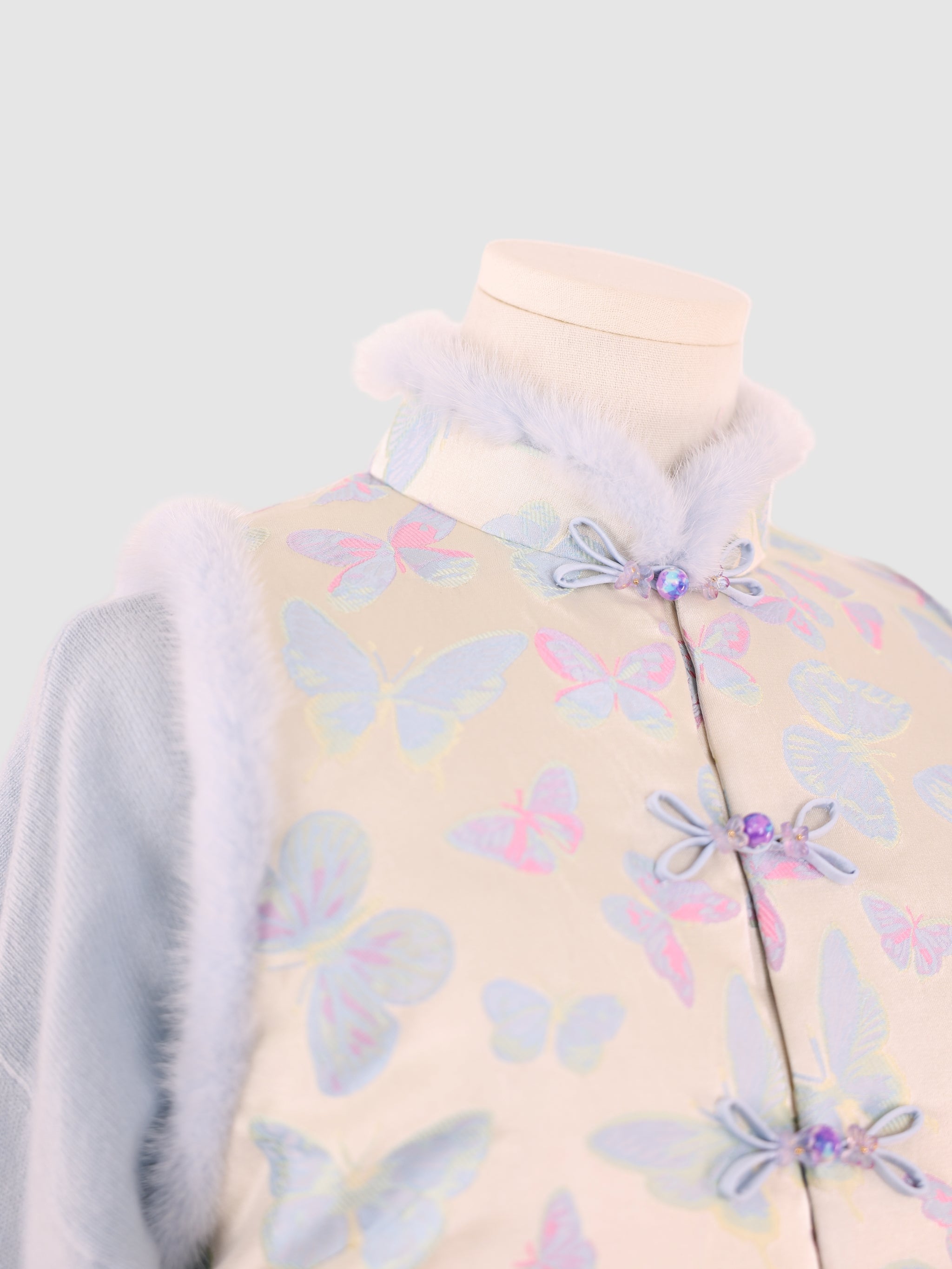 A close-up of the vest’s collar area with  mink trim, butterfly pattern, and decorative knot buttons.