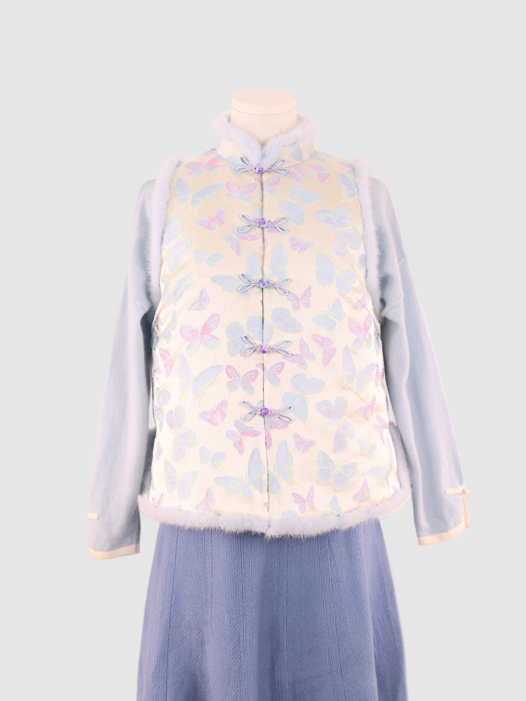 A close front view of the vest showing butterfly pattern, knot buttons, and  mink trim.