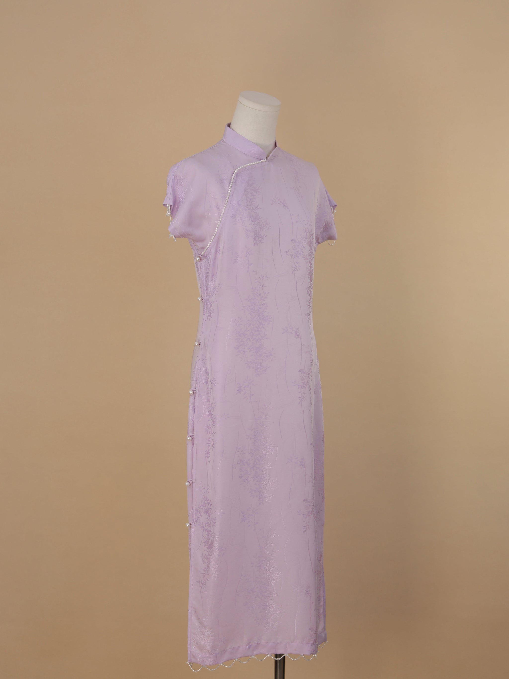 Full-length side-angled view of a lavender silk qipao featuring pearl button closures and scalloped hem.