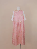 Full front view of a pink silk handmade qipao with gold floral jacquard, mandarin collar, pearl frog buttons, and mid-calf length skirt with sheer white sleeves.