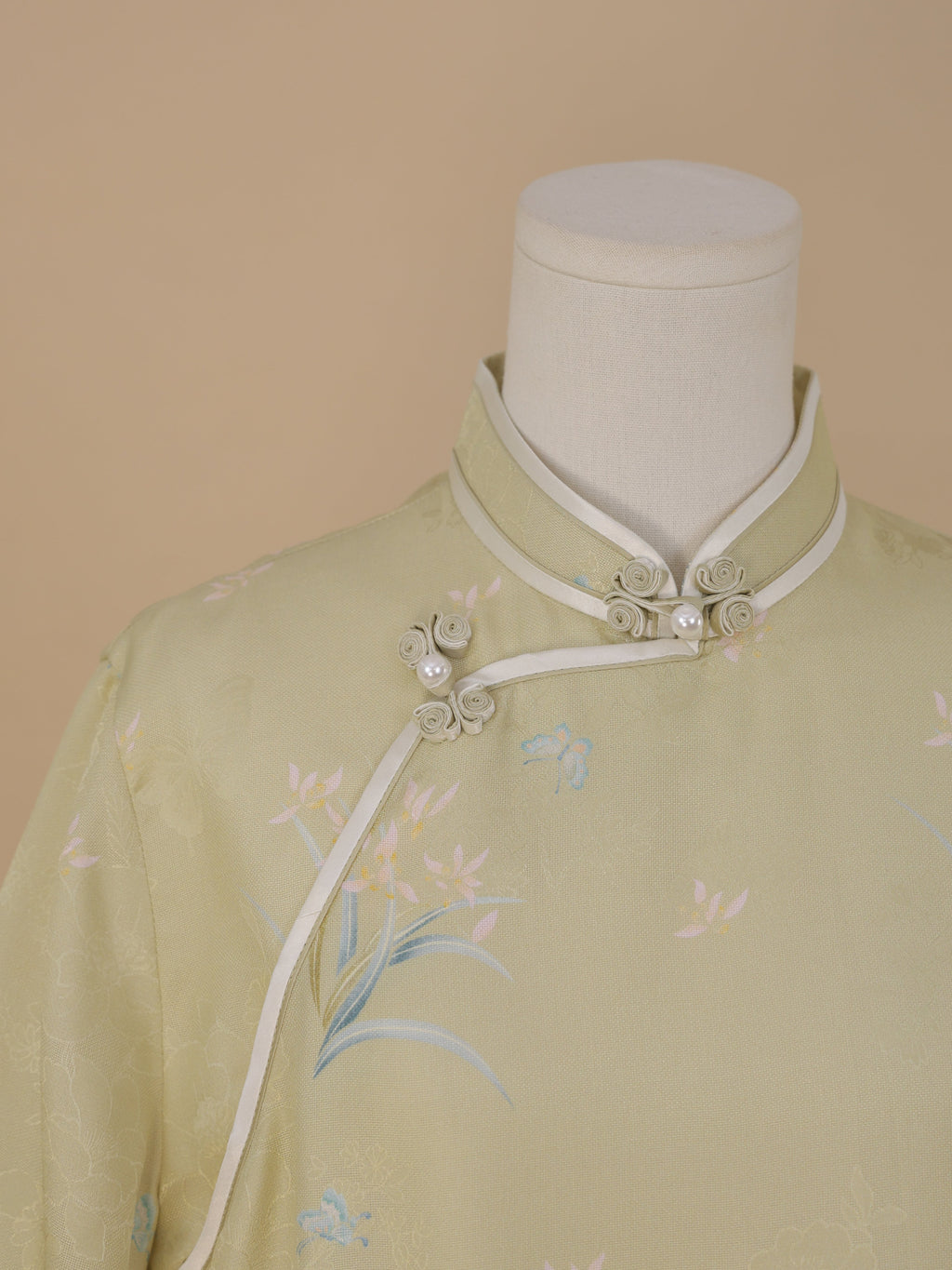 Close-up of the pale sage green qipao collar with white trim and delicate flower-shaped frog buttons accented with pearls.