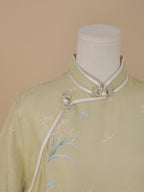 Close-up of the pale sage green qipao collar with white trim and delicate flower-shaped frog buttons accented with pearls.