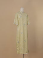 Full side view of a pale sage green short-sleeve qipao, mid-calf length, featuring floral and butterfly motifs, and white piping at the collar and hem.