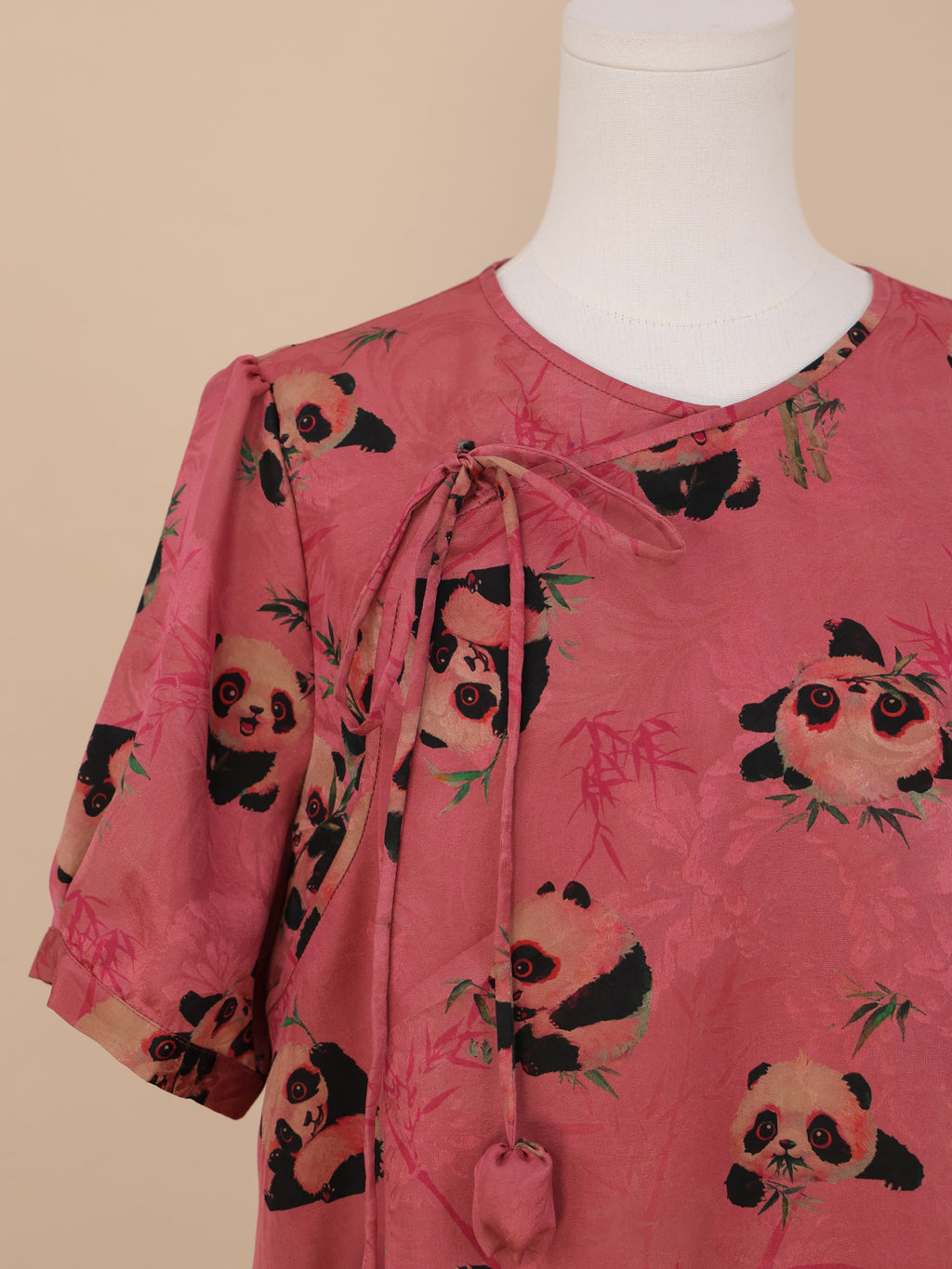 Close-up of the chest area, showing the hanging tie with fabric-covered ends, adorable panda prints with big round eyes, and a bamboo leaf motif in the background.
