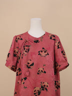 Front half-body view of a pink panda print short-sleeve dress, with a draping tie at the neckline and a relaxed sleeve design, fully covered in panda and bamboo prints.