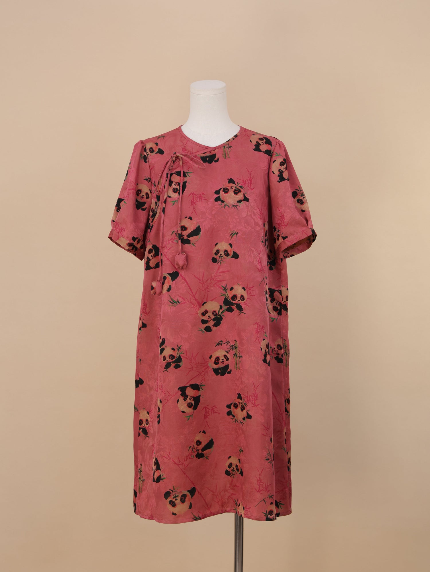 Full front view of a knee-length pink panda print short-sleeve dress in a loose straight silhouette, decorated with cartoon-style panda and bamboo prints.