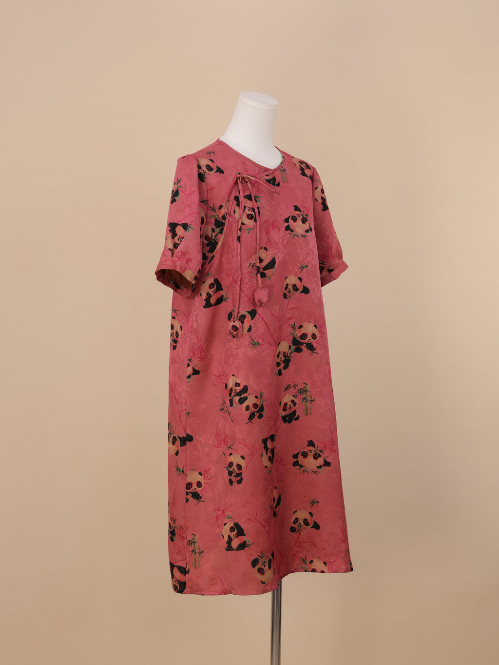 A pink short-sleeve dress featuring playful panda and bamboo prints, with a slender tie detail at the right neckline; knee-length design displayed in a side front angle.