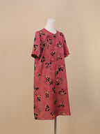 A pink short-sleeve dress featuring playful panda and bamboo prints, with a slender tie detail at the right neckline; knee-length design displayed in a side front angle.