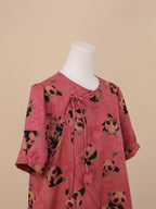 Close-up of the upper part of a pink panda print short-sleeve dress, showing round-faced panda and bamboo patterns, a tied neckline detail, and gently gathered sleeve ends.