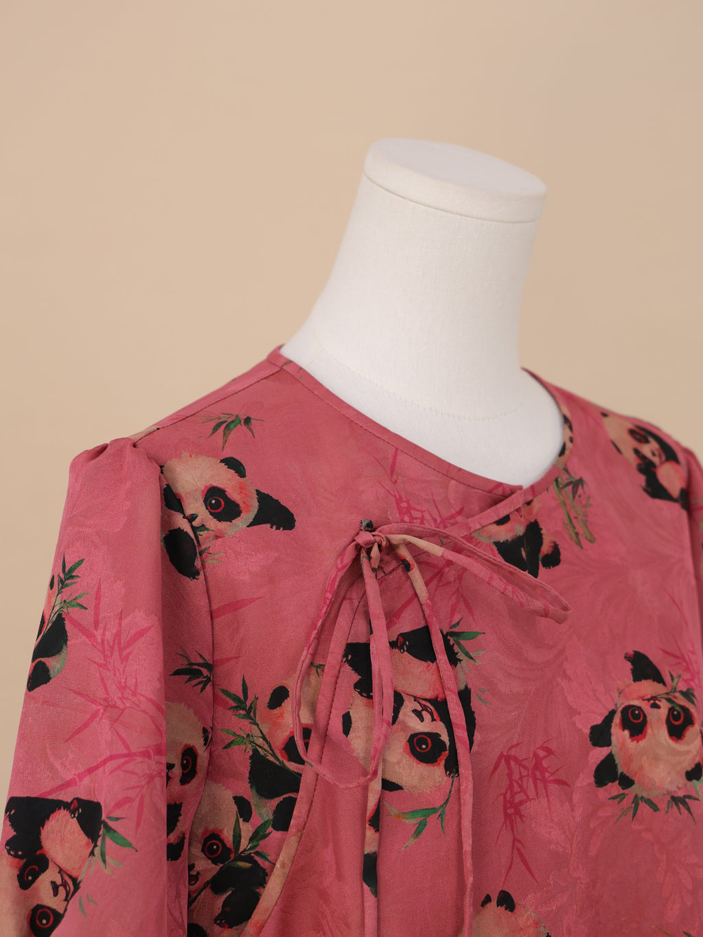 Detailed view of the neckline with overlapping tie strings, featuring multiple pandas in various poses against a soft pink bamboo-patterned background.