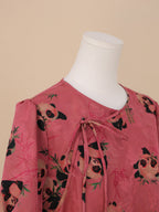 Detailed view of the neckline with overlapping tie strings, featuring multiple pandas in various poses against a soft pink bamboo-patterned background.