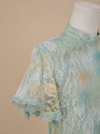 Detailed view of the right shoulder and short sleeve of a sea green lace cheongsam, with white floral lace, yellow and blue gradient accents, and scalloped lace edges.