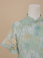 Detailed view of the shoulder and short sleeve of a sea green lace cheongsam, featuring white floral lace with yellow and blue gradient accents and delicate lace trim.