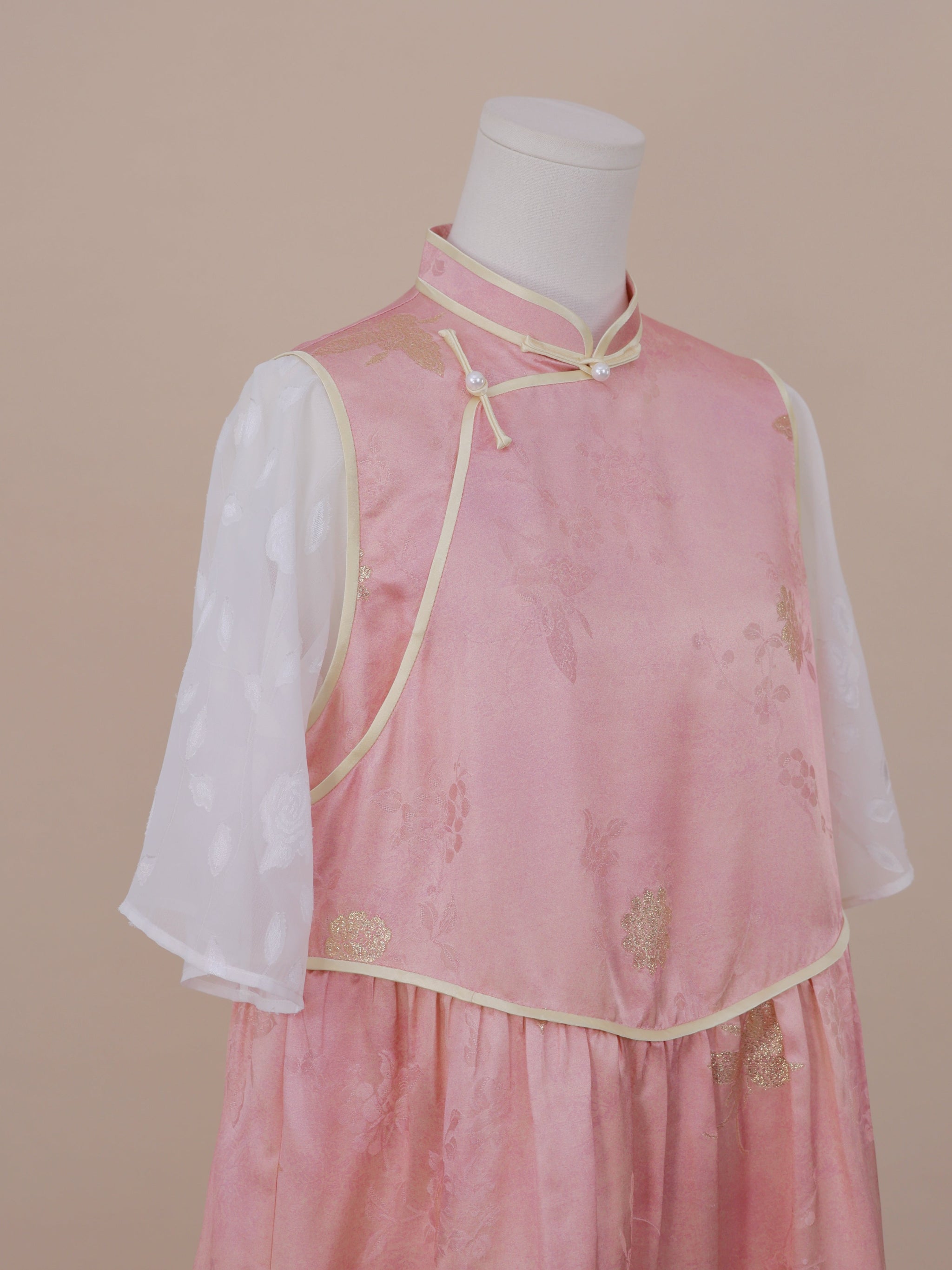 Side angle showing the diagonal frog button fastening and gold-trimmed edges of a pink silk qipao with sheer white sleeves for a soft, graceful look.