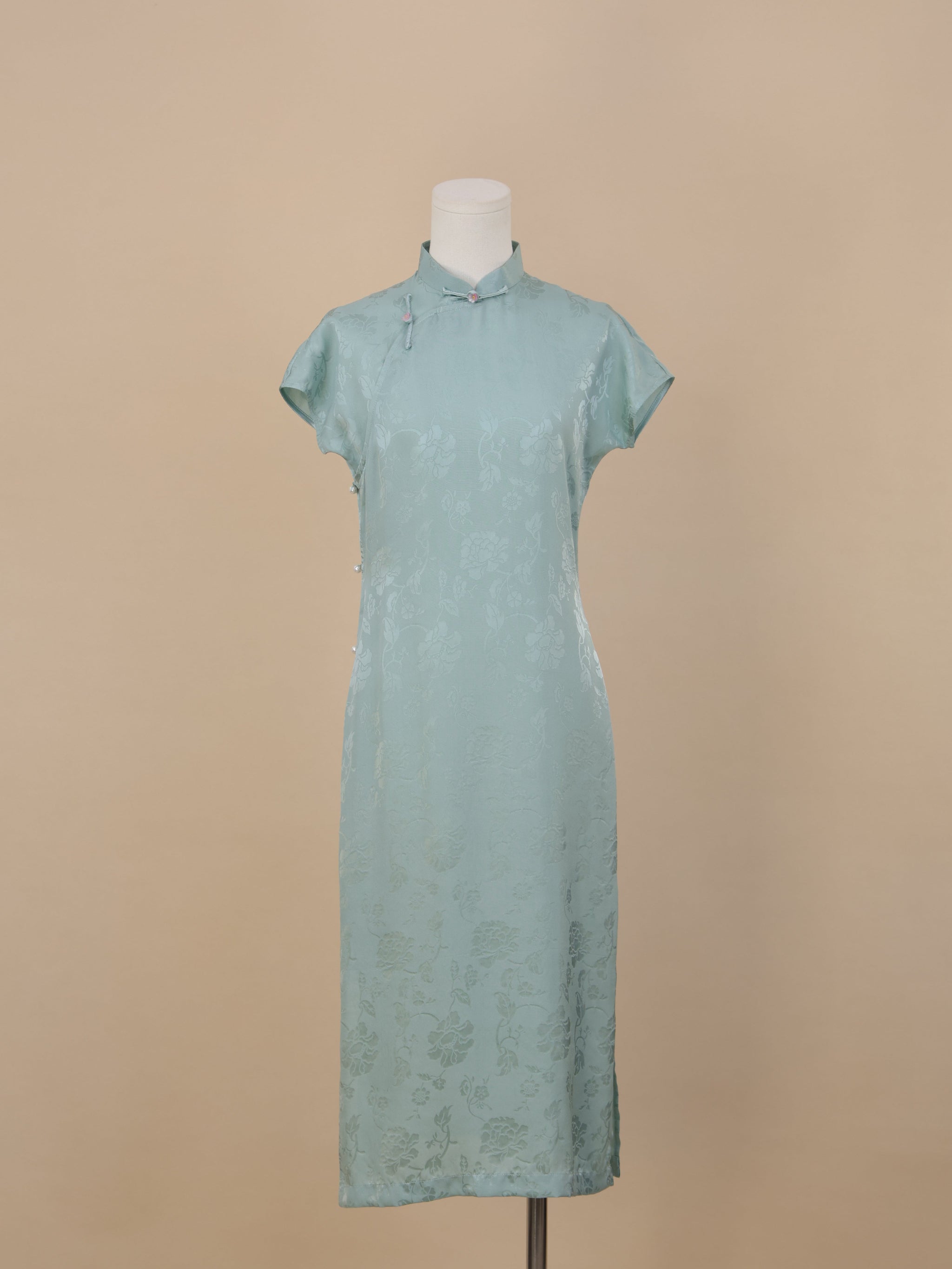 Full frontal view of a Celadon Blue silk cheongsam featuring short sleeves, Mandarin collar, floral jacquard pattern, and side pearl button accents.