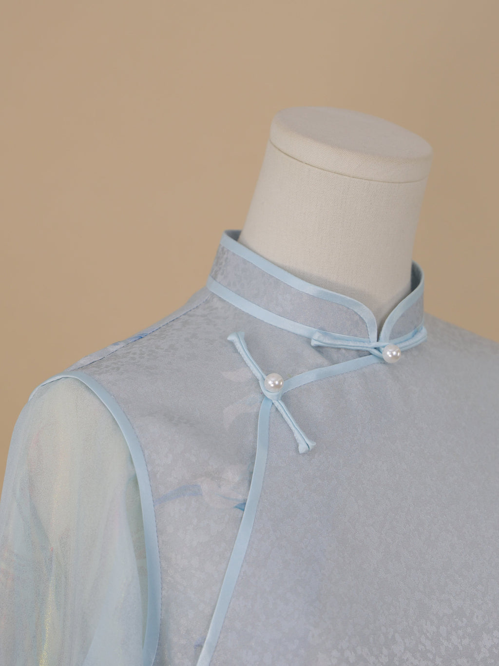 Collar detail of light blue silk cheongsam with orchid print, featuring classic stand collar and pearl button fastening.