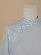 Close-up of the upper front of a light blue silk cheongsam, orchid print, sheer blue sleeves, and pearl buttons.