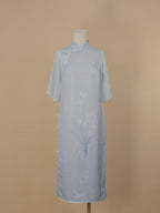 Full front view of light blue silk cheongsam, orchid print, faux two-piece design, mid-calf length, with side slits and pearl buttons.