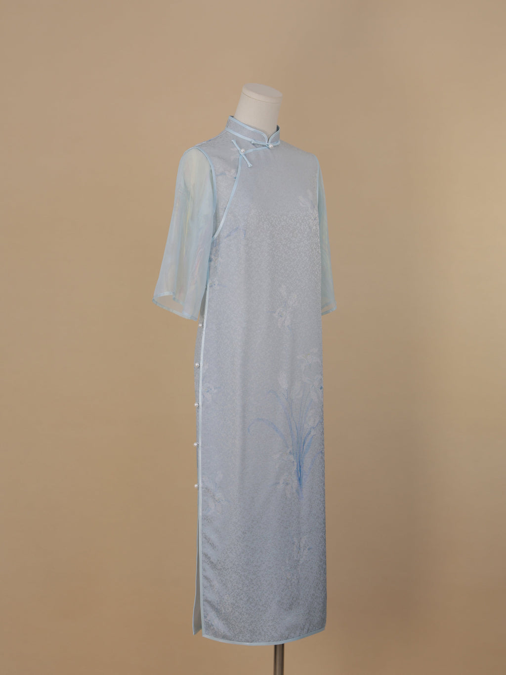 Light blue silk cheongsam with orchid print, faux two-piece design, side view, mid-calf length, pearl button closure.