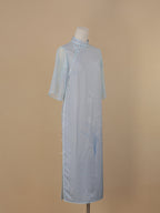 Light blue silk cheongsam with orchid print, faux two-piece design, side view, mid-calf length, pearl button closure.