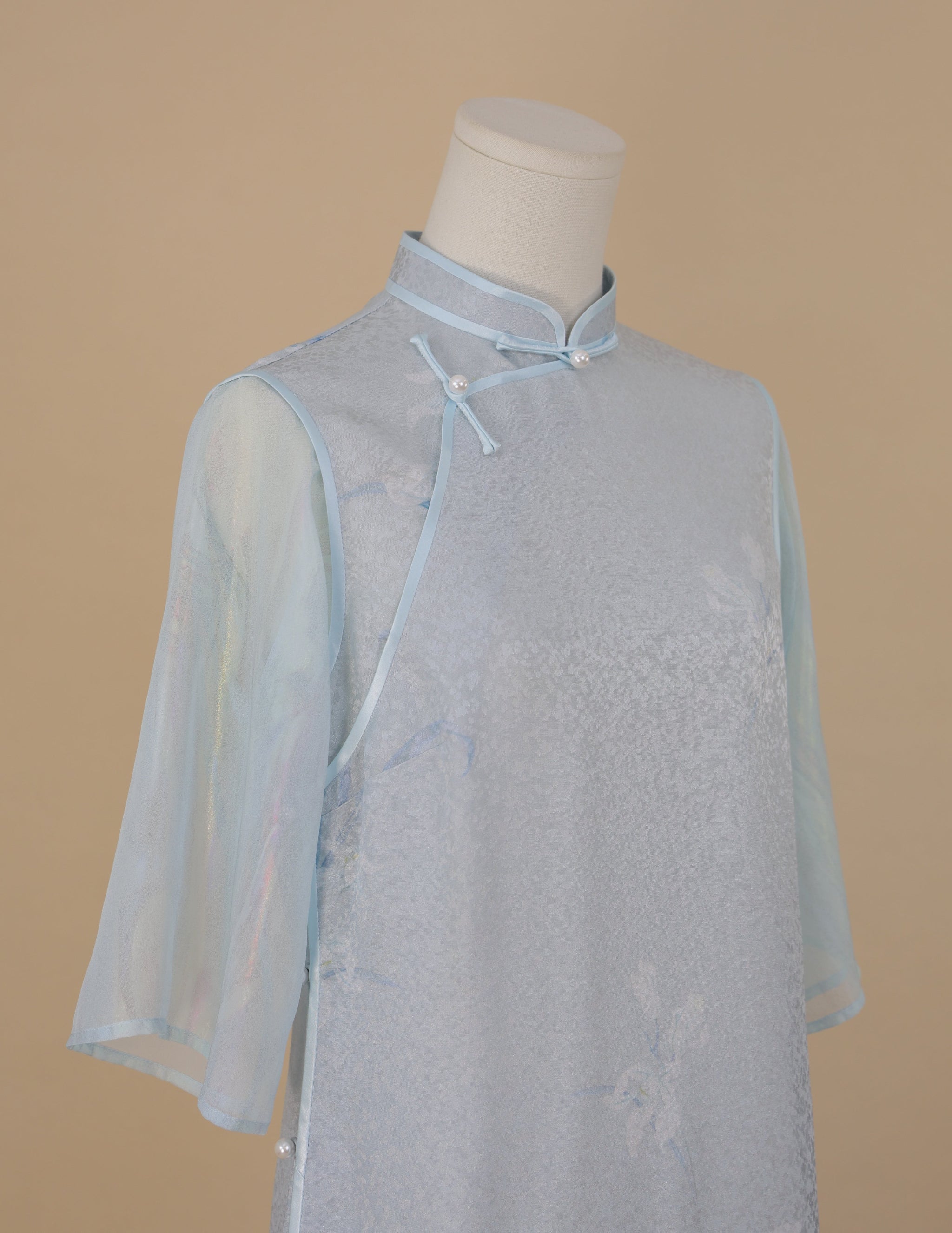 Close-up of light blue silk cheongsam showing orchid print, classic stand collar, and pearl button details.