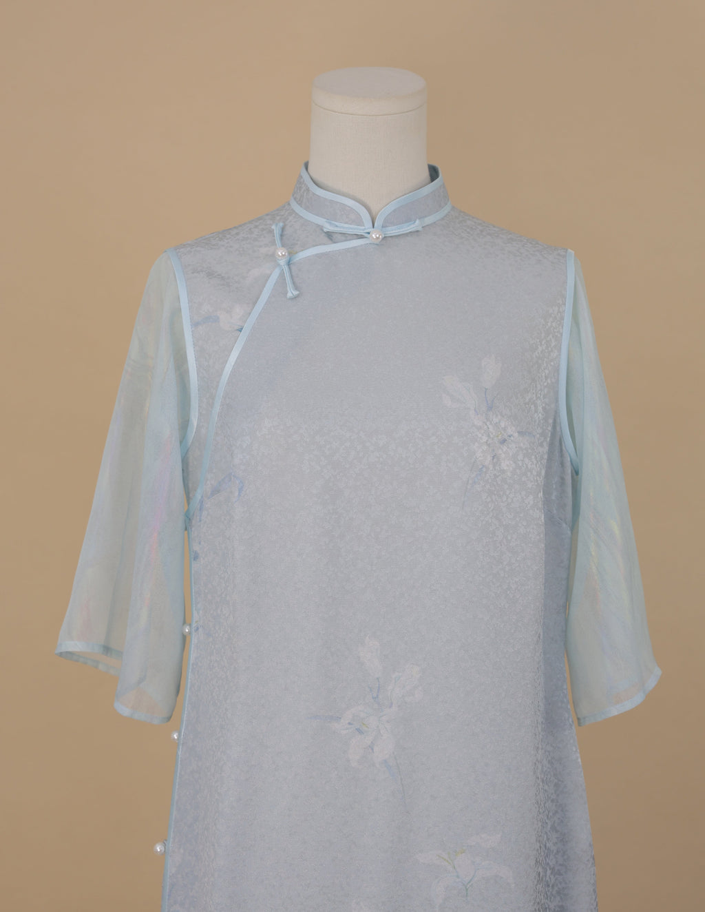 Front upper view of light blue silk cheongsam with orchid print, faux two-piece design, and sheer blue sleeves.