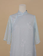 Front upper view of light blue silk cheongsam with orchid print, faux two-piece design, and sheer blue sleeves.