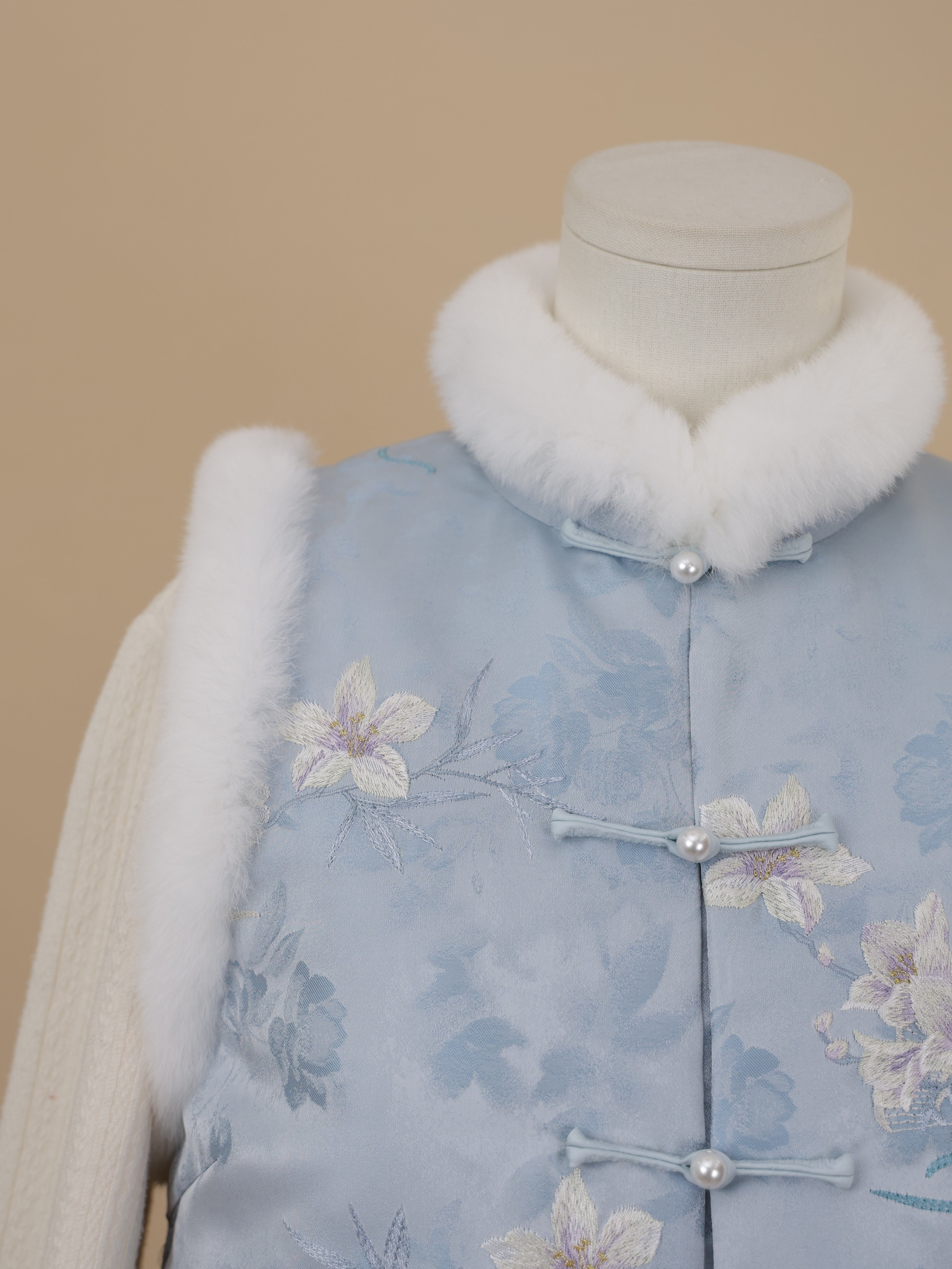 Close-up of tonal embroidery and white rabbit fur trim on a misty blue padded vest.