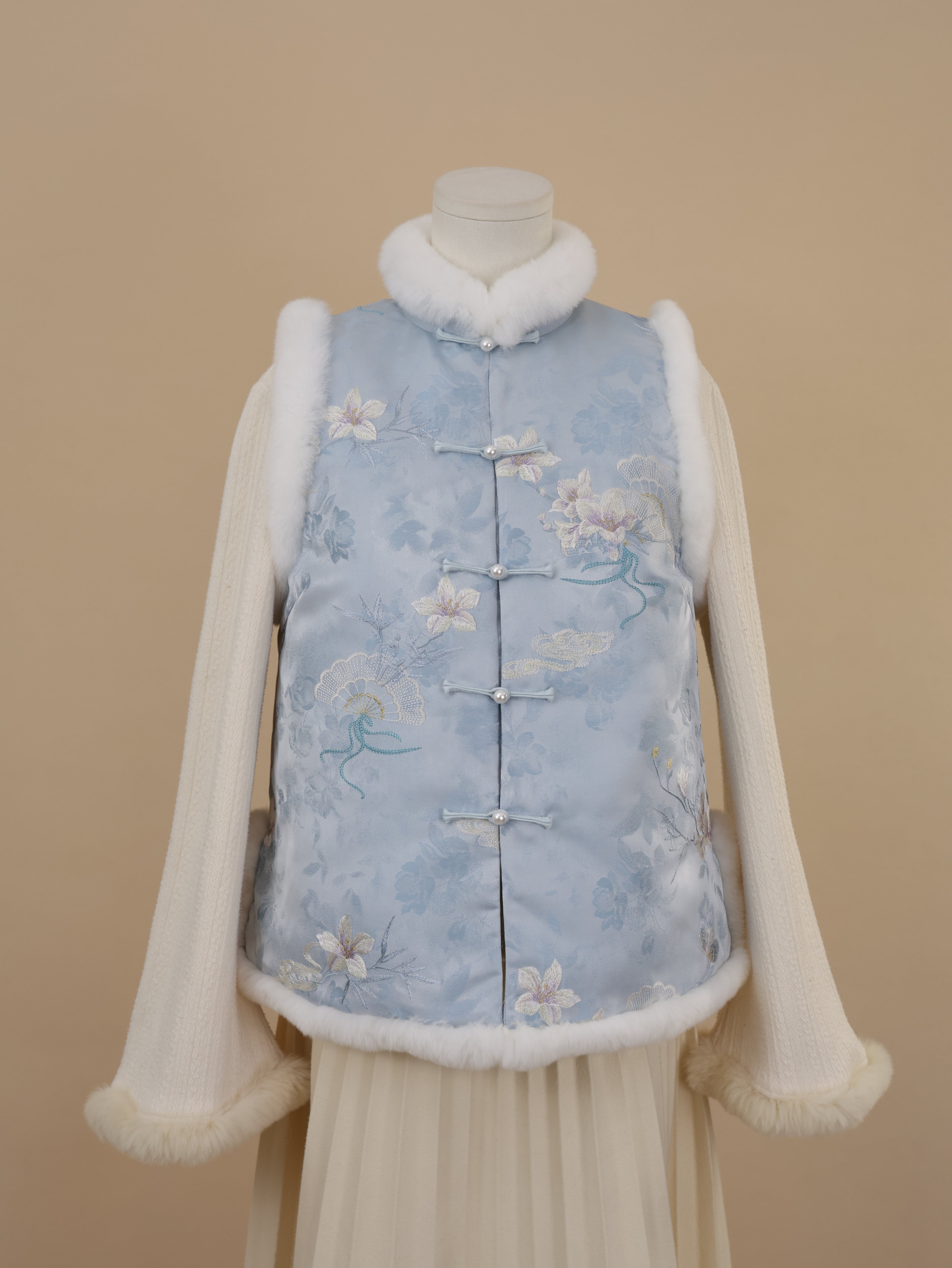 Front half view of a misty blue embroidered vest with white rabbit fur trim and straight frog-button closure.
