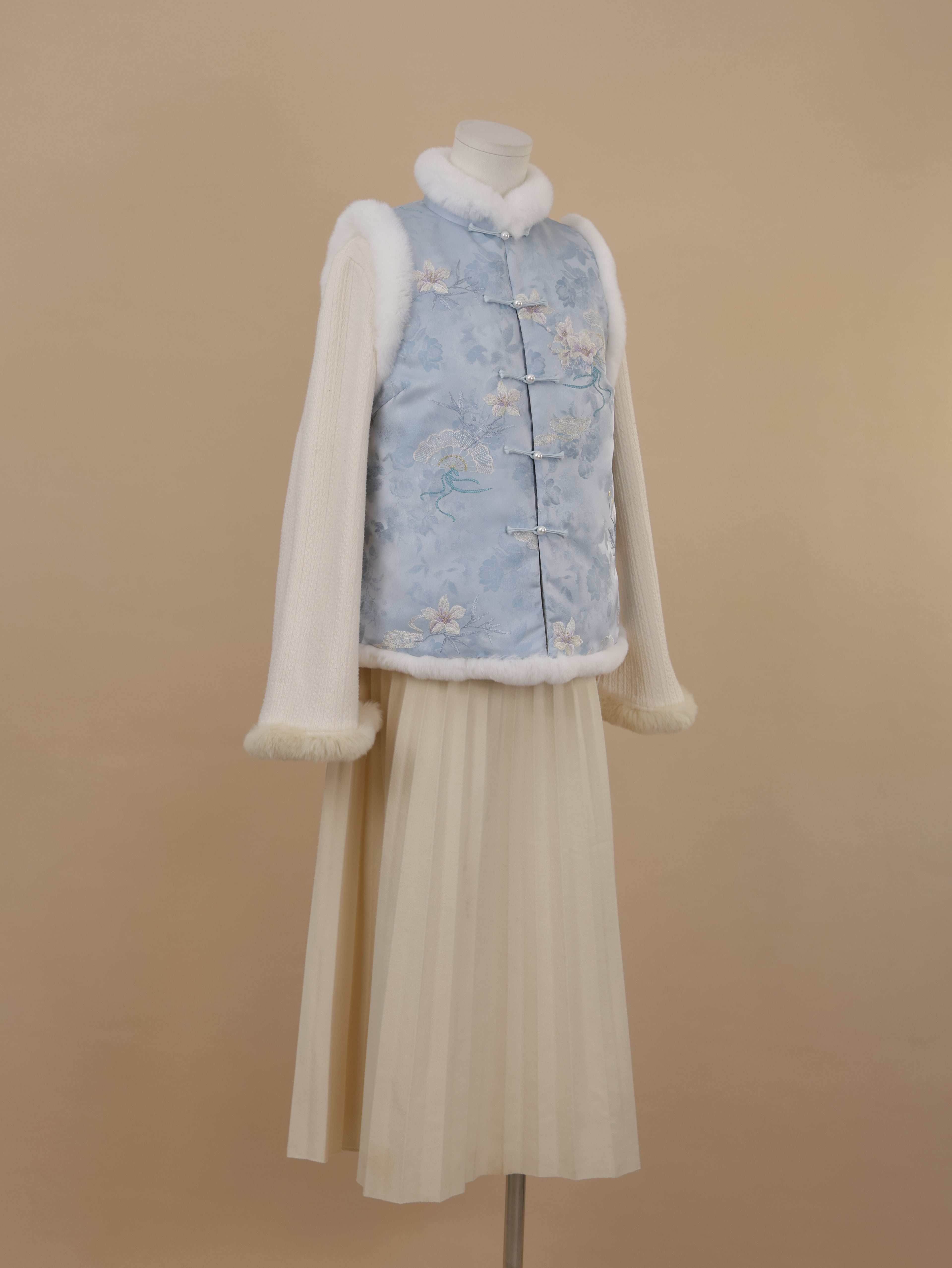 Side view of a misty blue embroidered vest featuring white rabbit fur trim and silkly cotton padding.