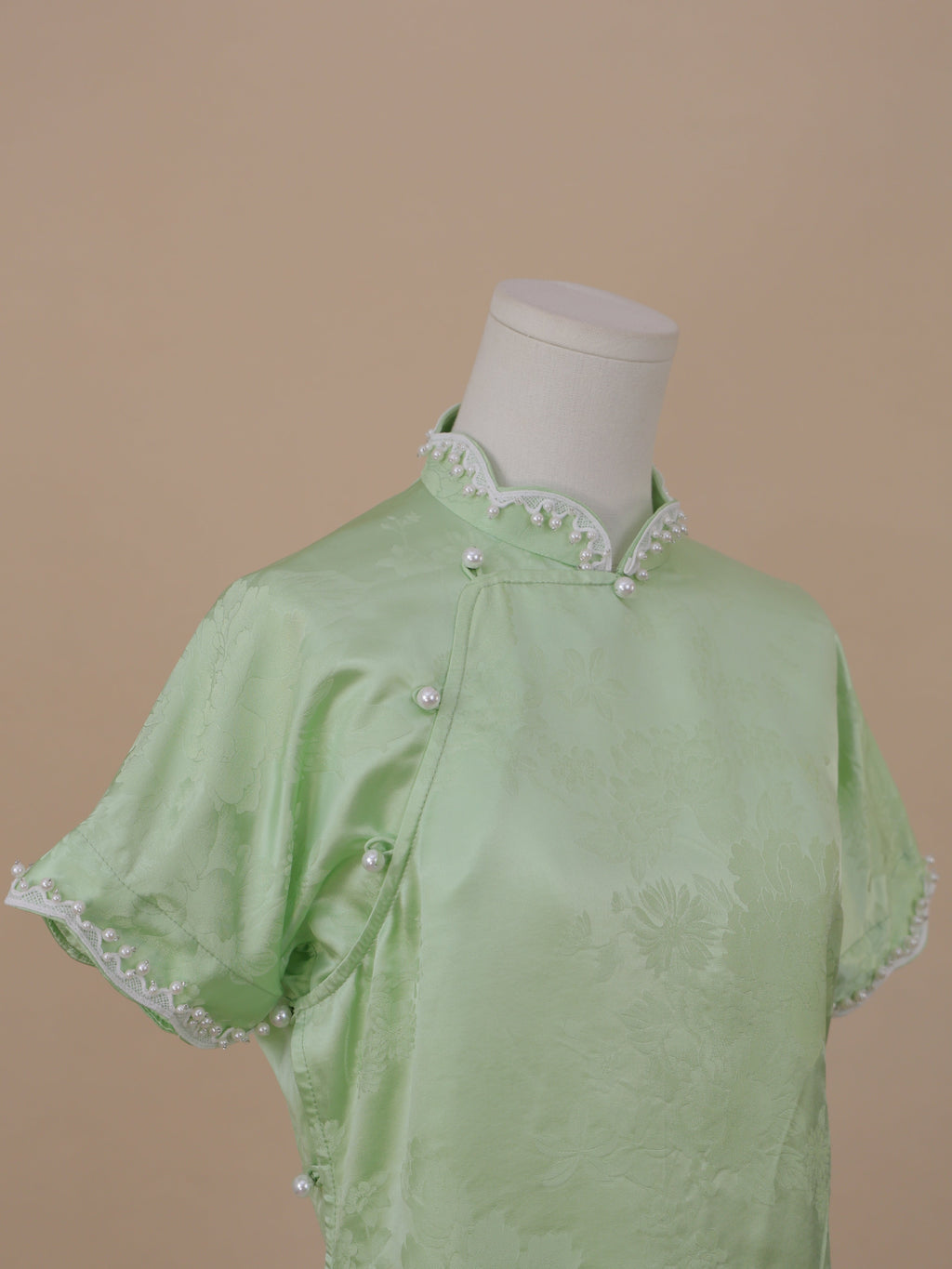 Close-up of pale green silk qipao with classic stand collar and pearl trim details