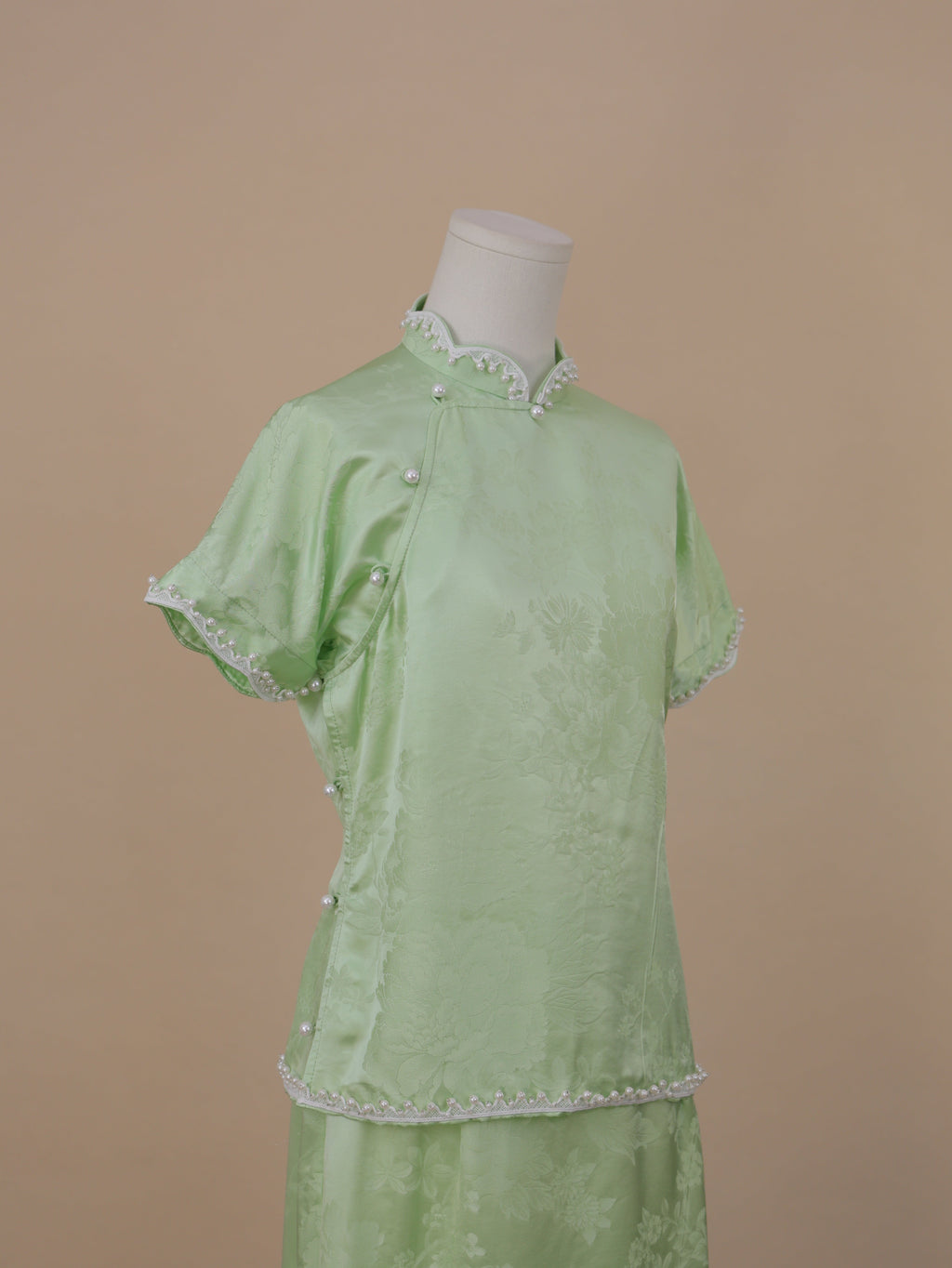 Half-length side view of pale green silk qipao highlighting pearl trim and jacquard texture