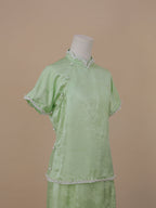Half-length side view of pale green silk qipao highlighting pearl trim and jacquard texture