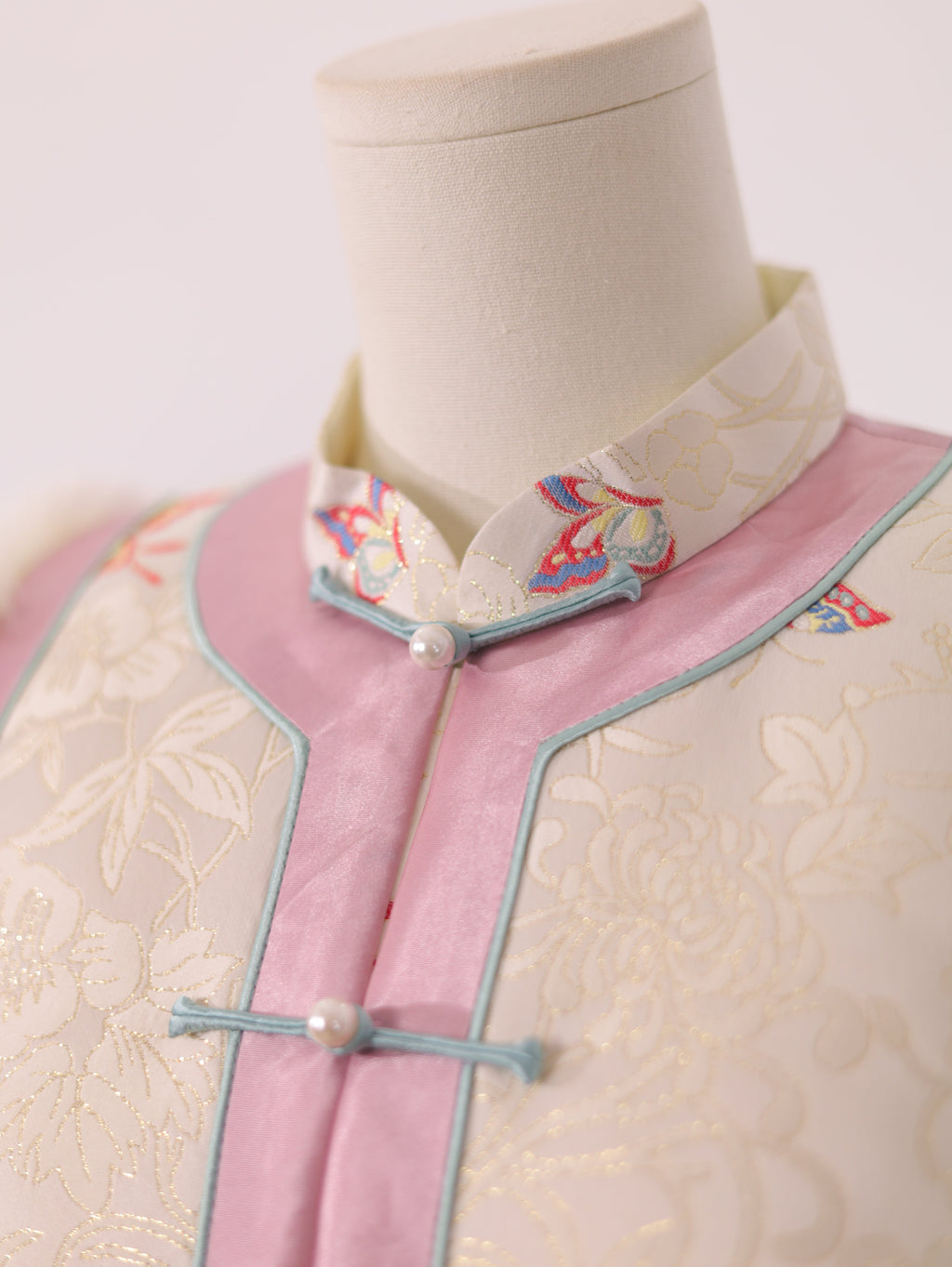 Close-up of frog button closure and collar detail on pink and white butterfly vest