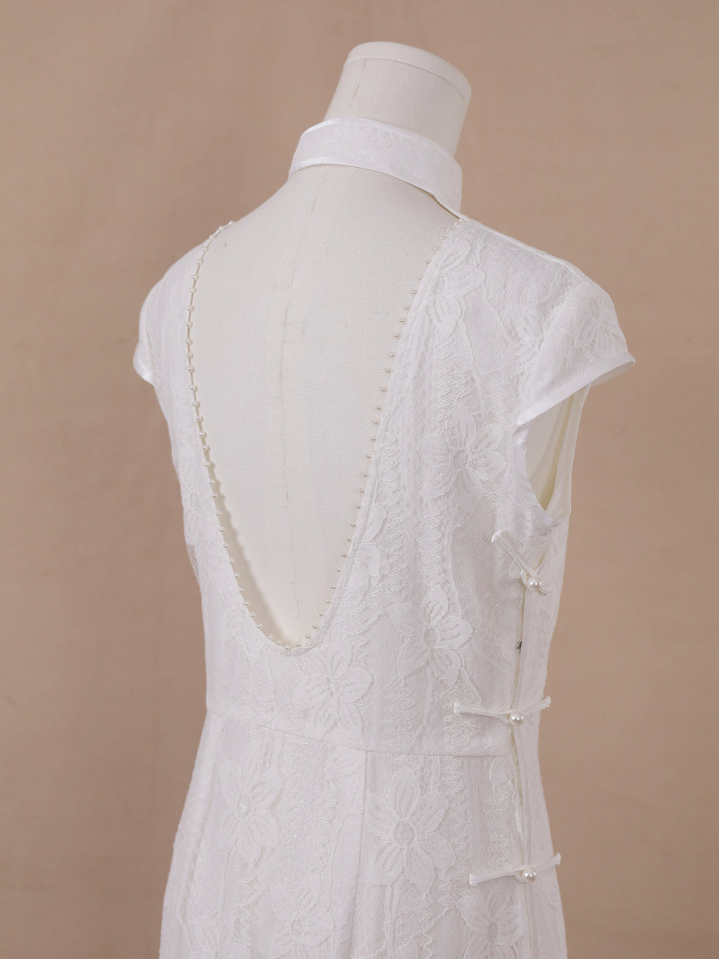 Backless detail of white lace qipao cheongsam with deep V open back and pearl embellishment.
