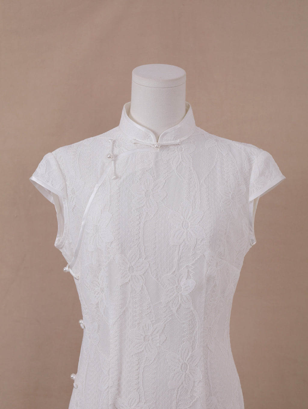 Close-up of handmade white lace qipao cheongsam with mandarin collar and pearl button side closure.